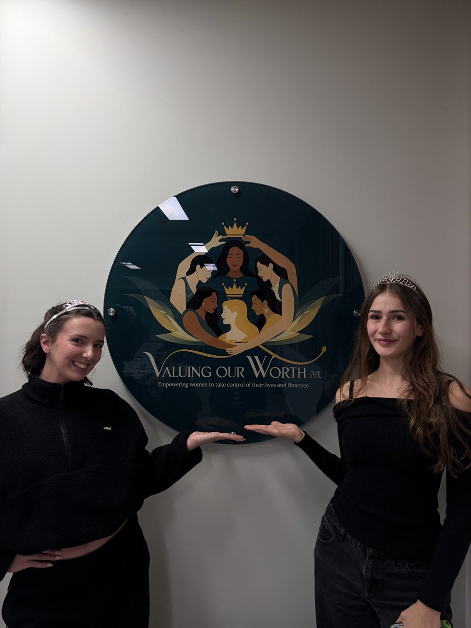 Two young women standing beside the Valuing Our Worth sign