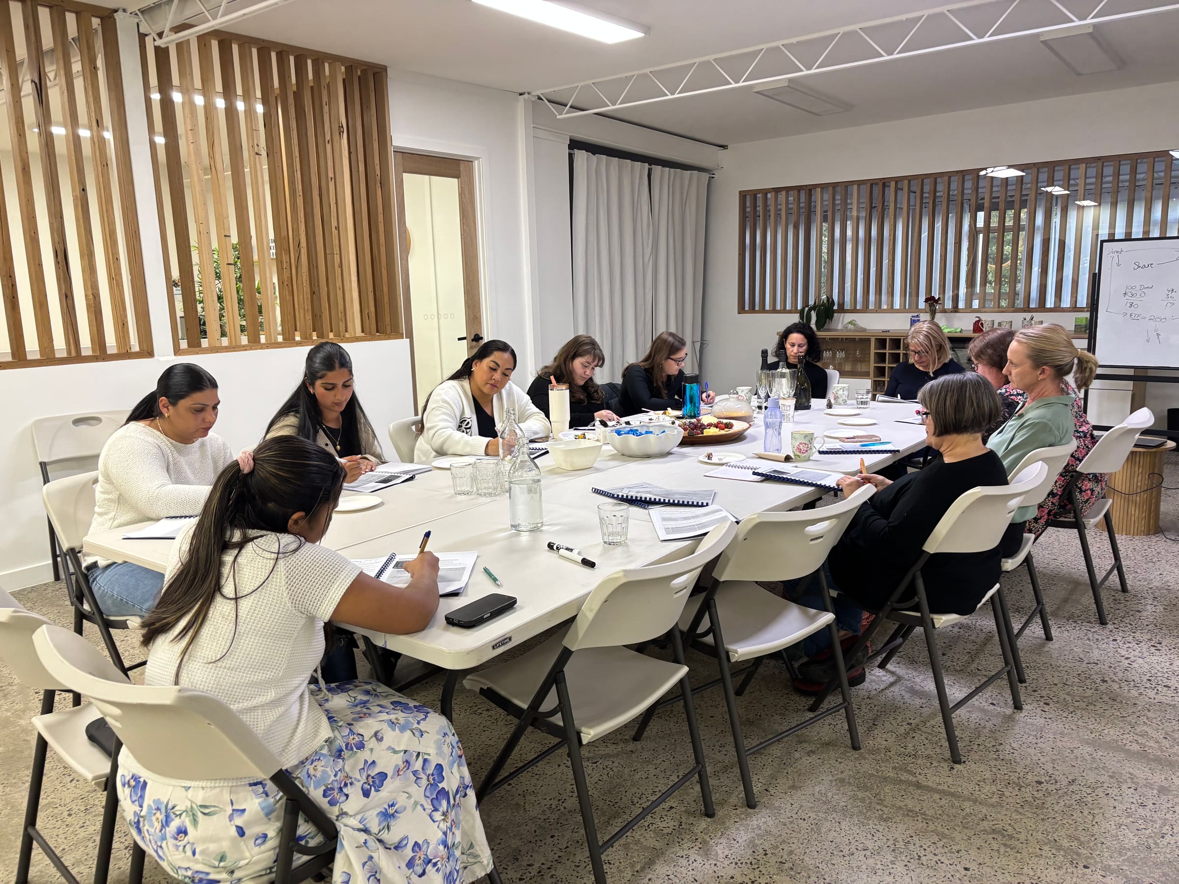 Ten women gathered around a conference table with workbooks during a Financially Fit Females workshop session
