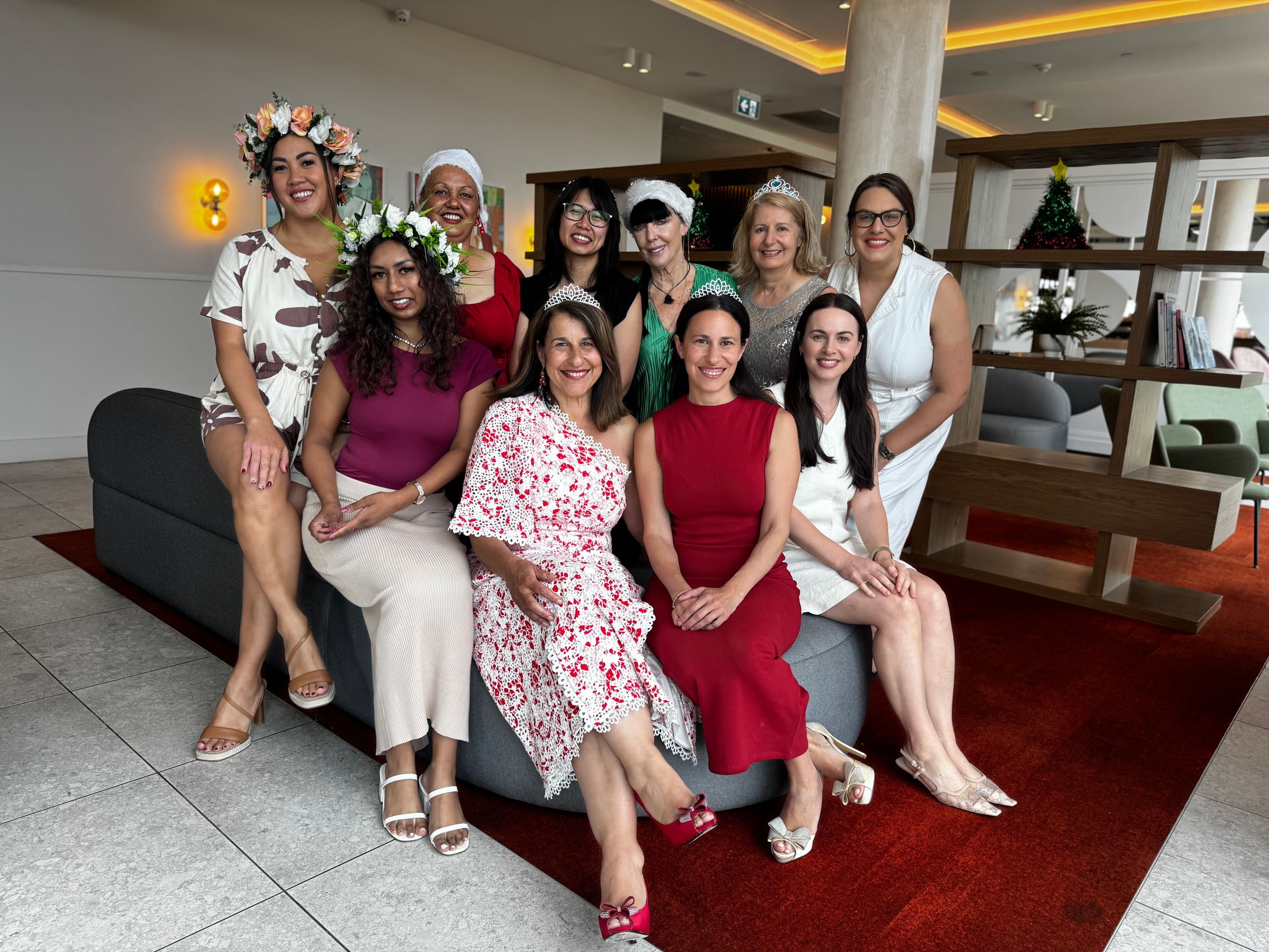 A festive group of women celebrating together, some wearing flower crowns and tiaras, at a Valuing Our Worth community event